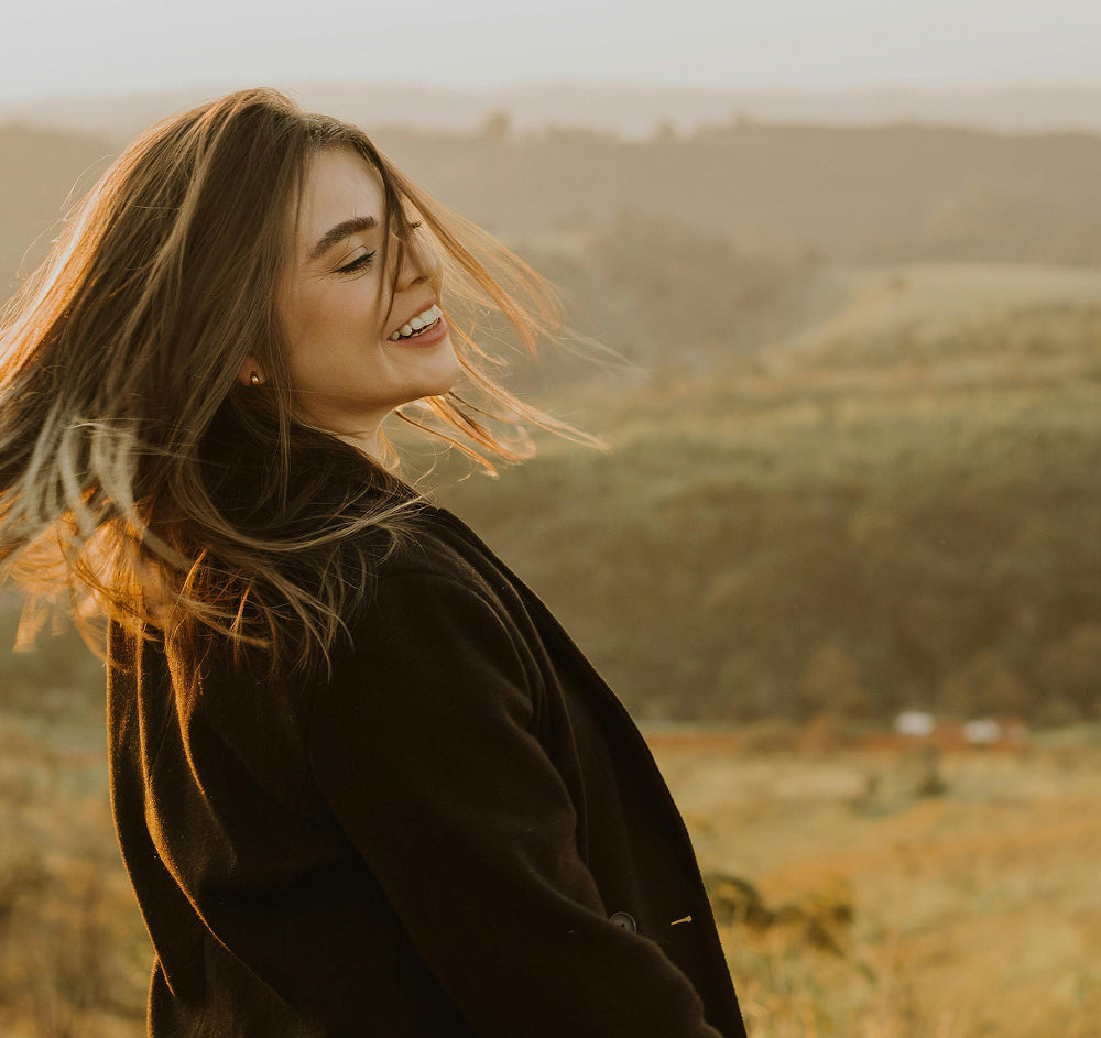Femme souriant de profil face à un paysage vallonné ensoleillé